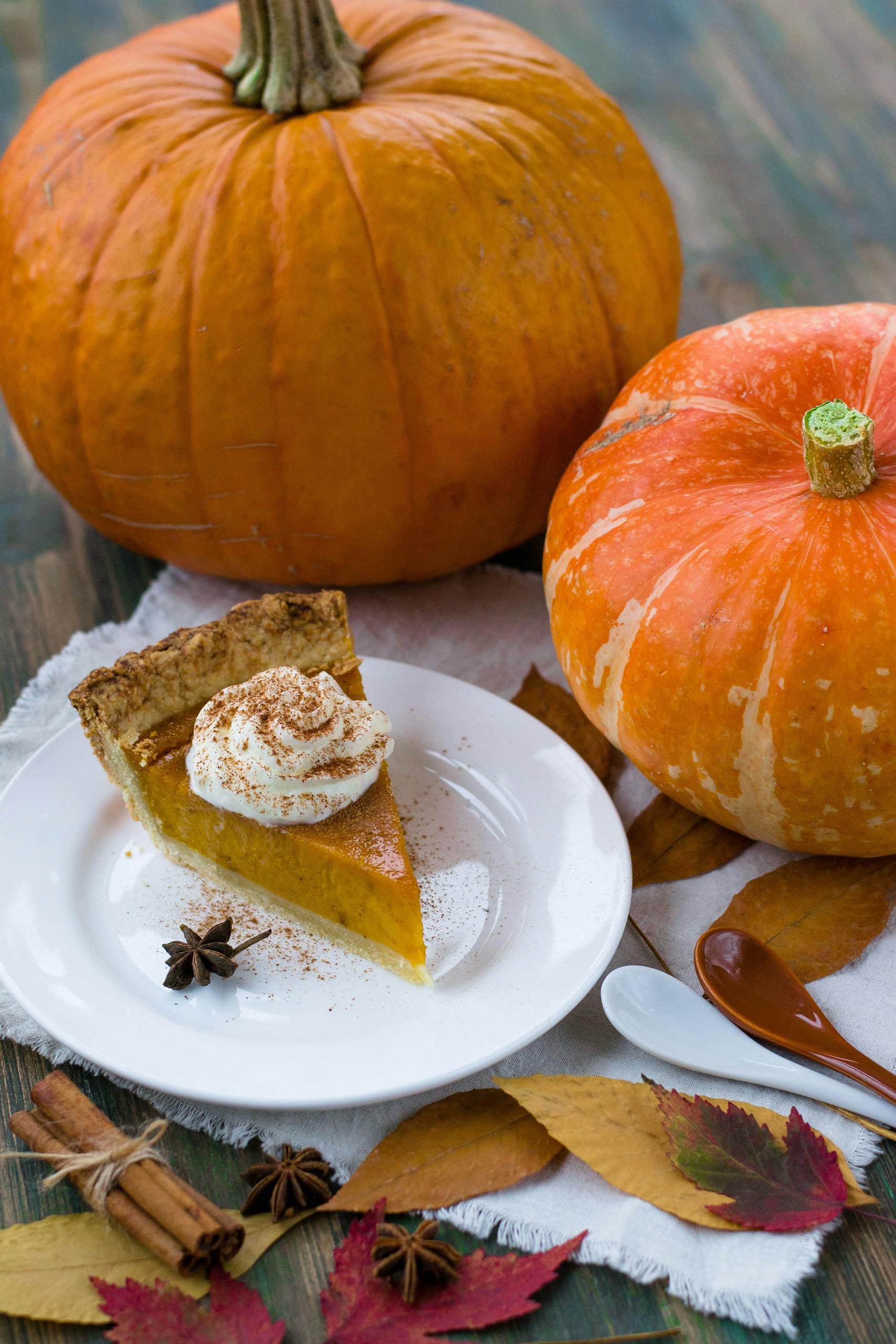 Slice of pumpkin pie with whipped cream, surrounded by pumpkins and autumn leaves, perfect for fall celebrations.